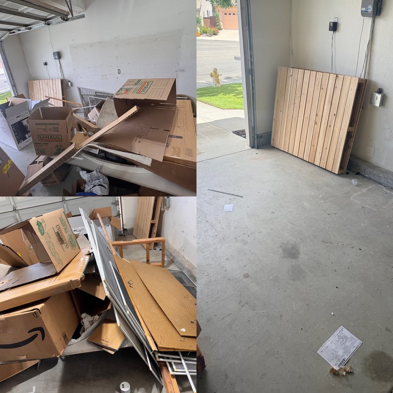 Garage interior showing cardboard boxes and wooden materials scattered on concrete floor, with stacked plywood sheets leaning against wall