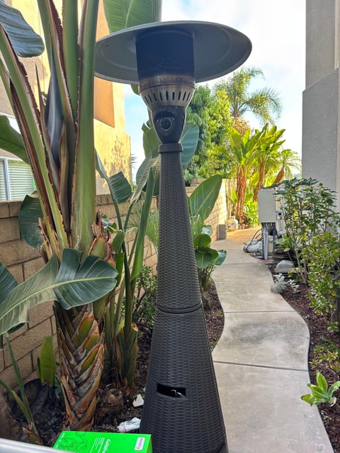 Black outdoor patio heater surrounded by tropical plants and palm trees in a residential garden setting