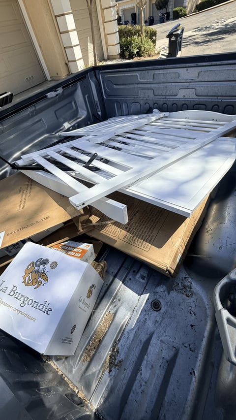 Pickup truck bed with white metal shelving unit and cardboard boxes stacked during delivery or moving
