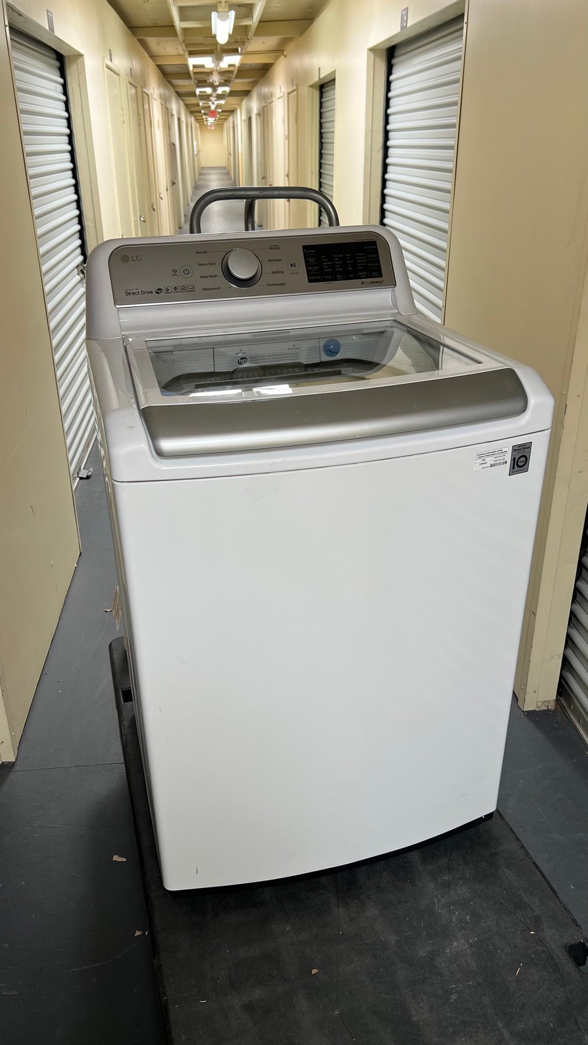 White top-load washing machine in a storage unit hallway with metal doors on both sides
