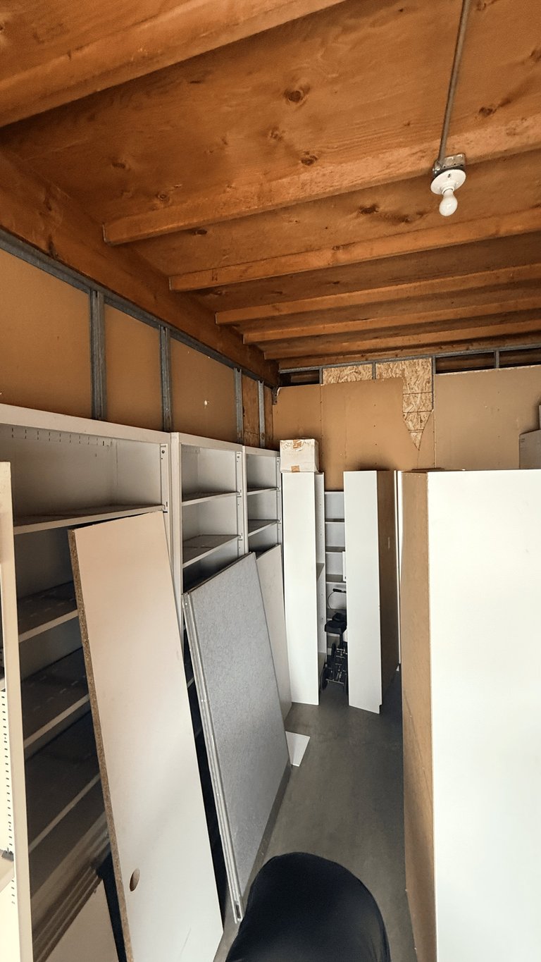 Interior storage area with wooden ceiling beams, metal shelving units, and white panels stacked against walls