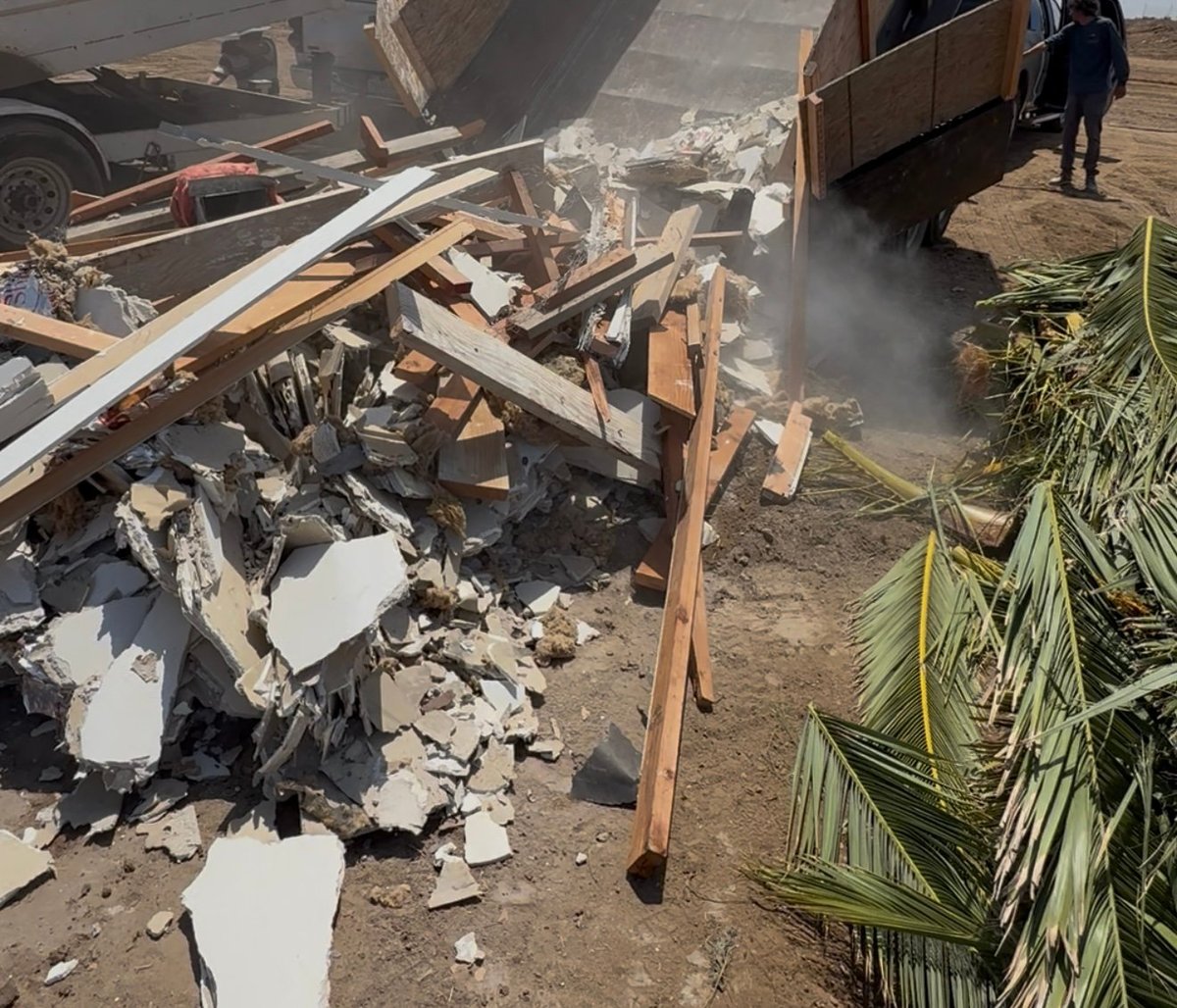 Debris and rubble scattered on ground with wooden beams, white materials, and trucks at a demolition or waste disposal site